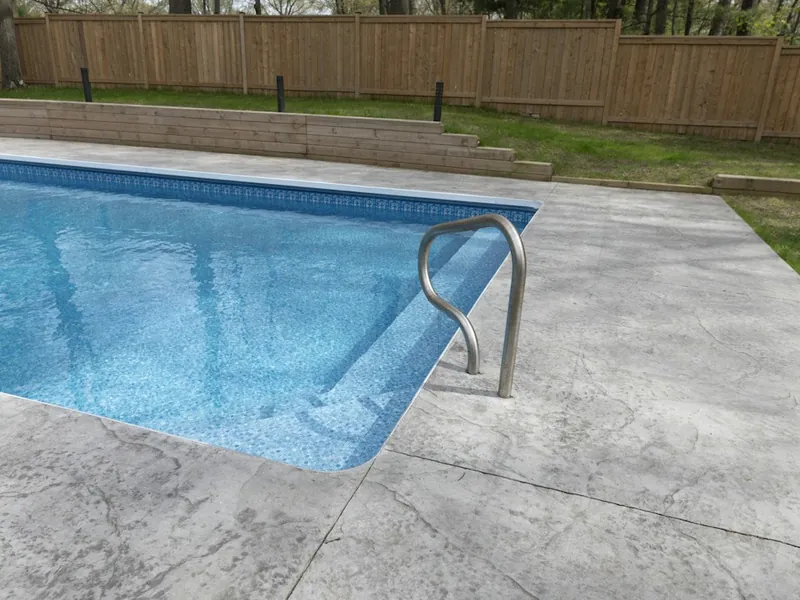 Rectangular backyard pool with a gray concrete deck and wood fence in San Marcos